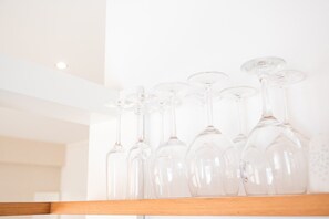 Une collection de verres à vin transparents, disposés sur une étagère en bois, devant un mur blanc.