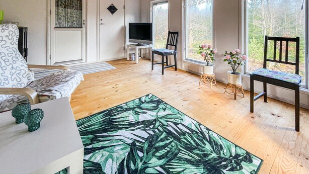 Uma sala de estar aconchegante com sofá, mesa de centro, TV e janela com vista para árvores.