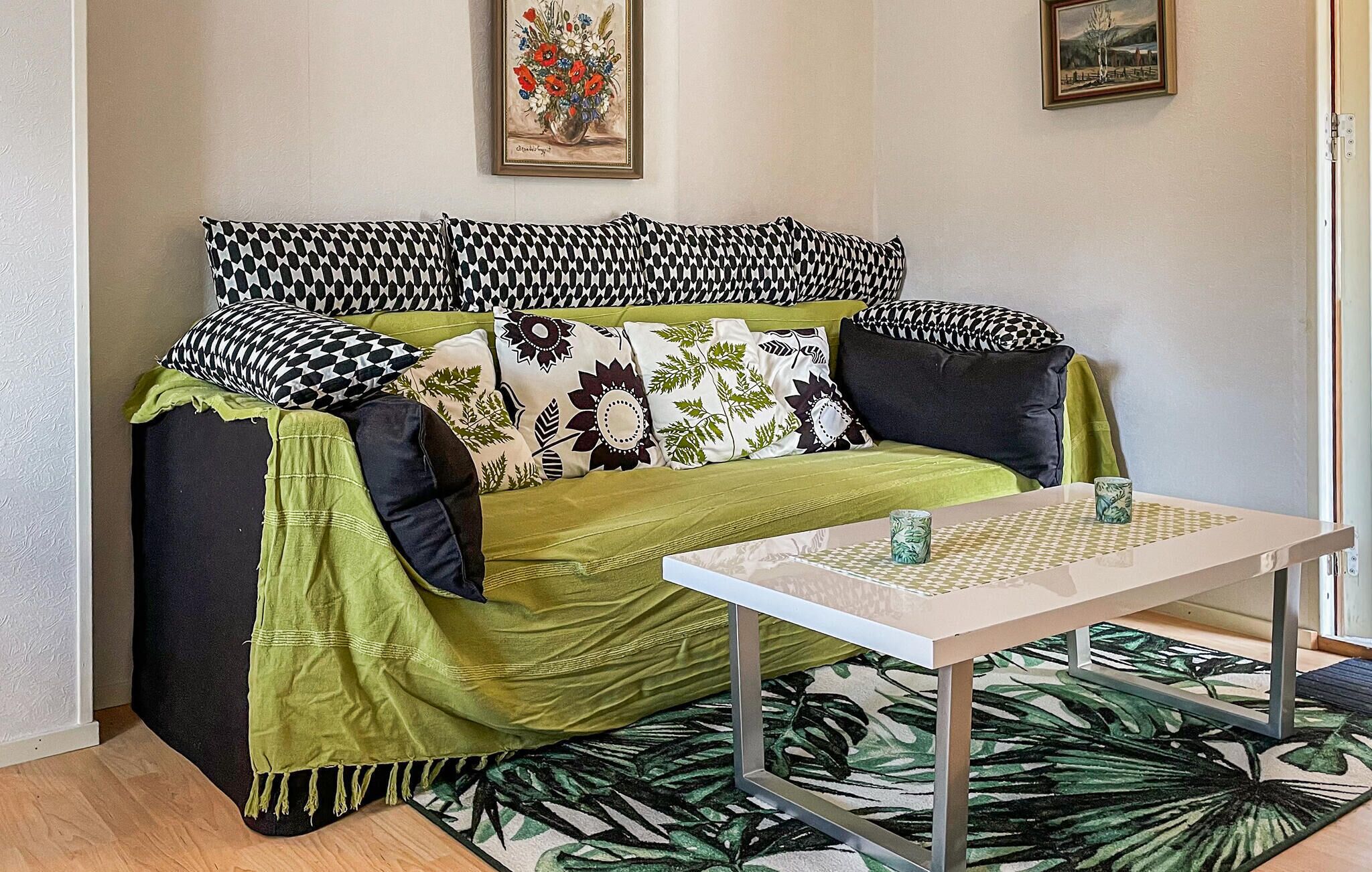 Um sofá com almofadas estampadas, um cobertor verde e uma mesa com dois copos.