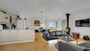 Une cuisine moderne avec des meubles blancs, un coin repas avec une table et des chaises, un canapé en cuir noir et un poêle à bois.