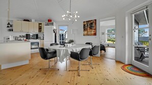 Une cuisine moderne avec des meubles blancs, un coin repas comprenant une table ronde et des chaises noires, un lustre et une grande fenêtre donnant sur l’extérieur.