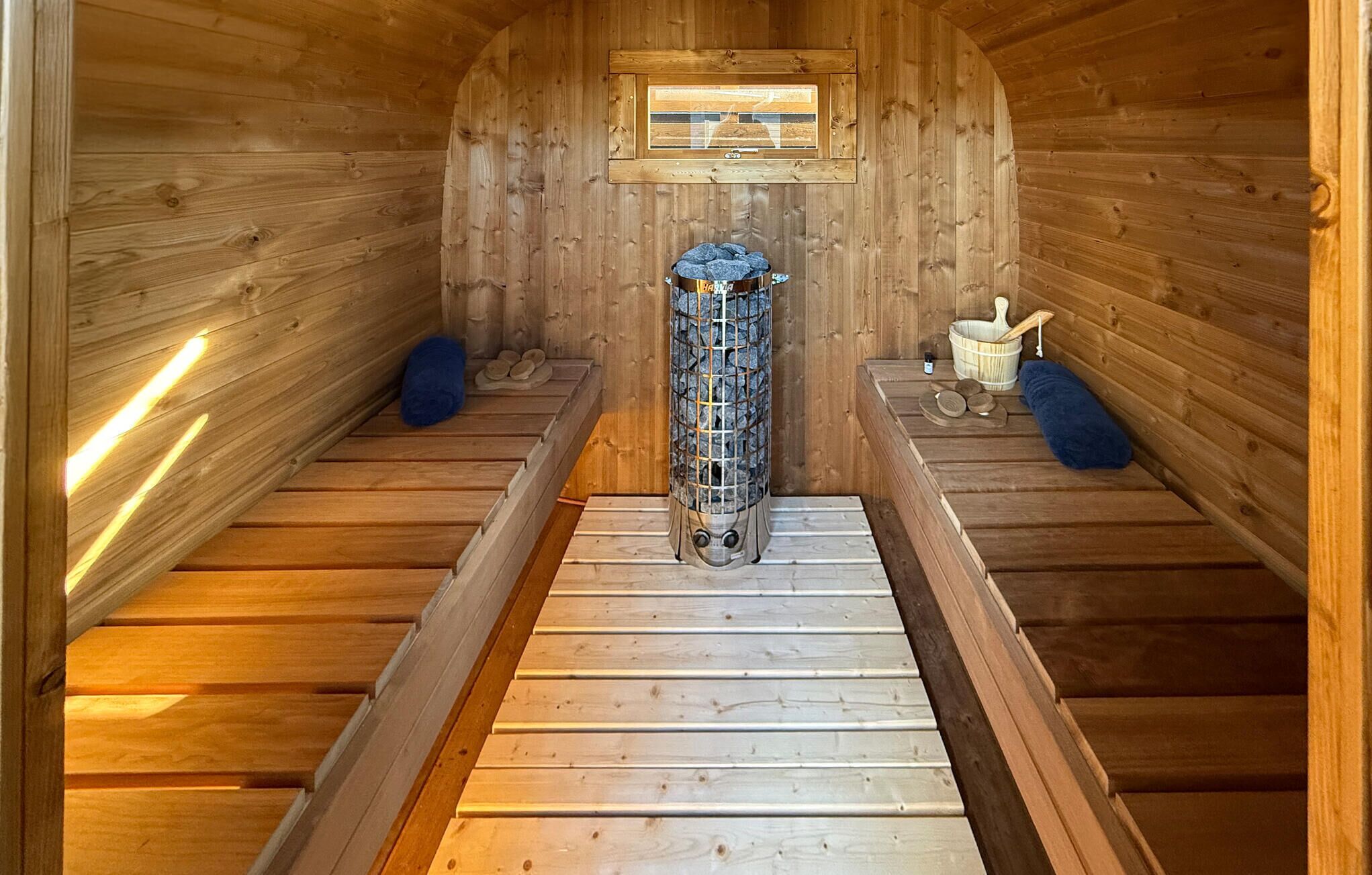 A sauna room with wooden walls, a central stone heater, and benches on either side.