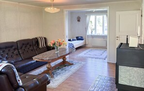 A living room with a dark brown leather sofa, a marble coffee table with a vase of flowers, a wooden door, and a black appliance on the right. - Awesome home in Hamburgsund with WiFi (Hamburgsund)