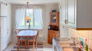 A kitchen with a dining table, chairs, a hanging light fixture, a cabinet with a stove, and a window with curtains. - Awesome home in Hamburgsund with WiFi (Hamburgsund)