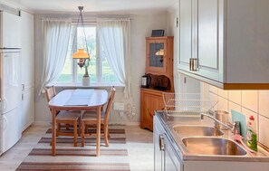 A kitchen with a dining table, chairs, a hanging light fixture, a cabinet with a stove, and a window with curtains. - Awesome home in Hamburgsund with WiFi (Hamburgsund)