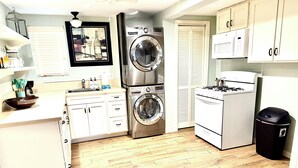 A compact kitchen with a washing machine, stove, microwave, and white cabinets. - Walking distance to the Beach! 2 kitchens! Ground floor access! (Galveston)