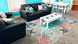 A living room with a dark sofa, a white coffee table, and a colorful rug. - Walking distance to the Beach! 2 kitchens! Ground floor access! (Galveston)