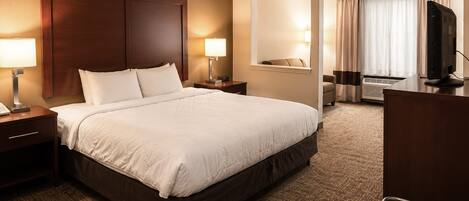 A hotel room with a large bed, bedside tables with lamps, a desk with a computer, a chair, and a view of the outside through a window.
