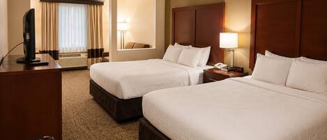 A hotel room with two beds, a desk with a TV, a chair, and a lamp.