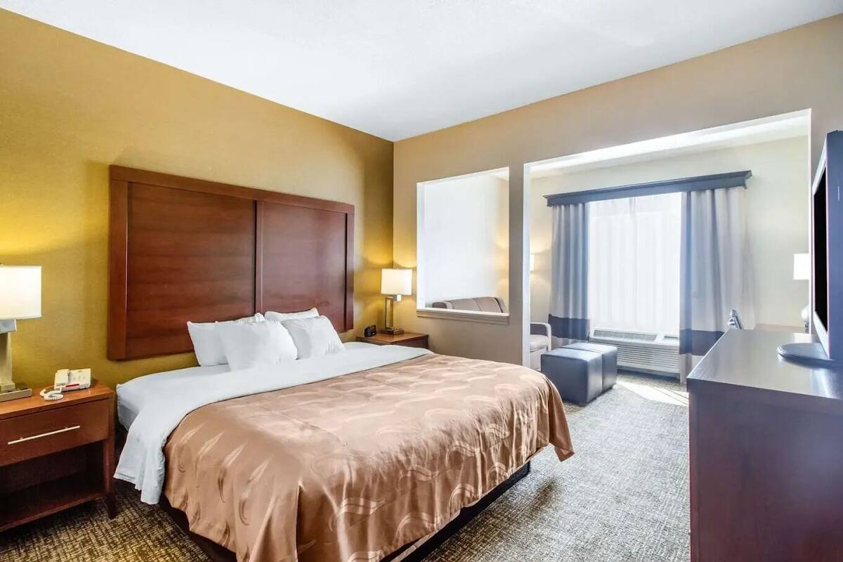 Ein Hotelzimmer mit einem großen Bett, Nachttischen, einem Schreibtisch, einem Sessel und Blick ins Freie.