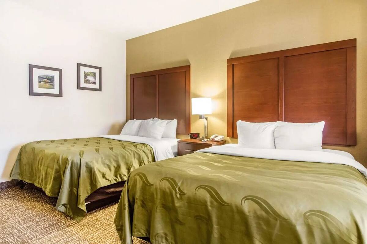 Ein Hotelzimmer mit zwei Betten, einem Nachttisch mit Lampe und zwei gerahmten Bildern an der Wand.