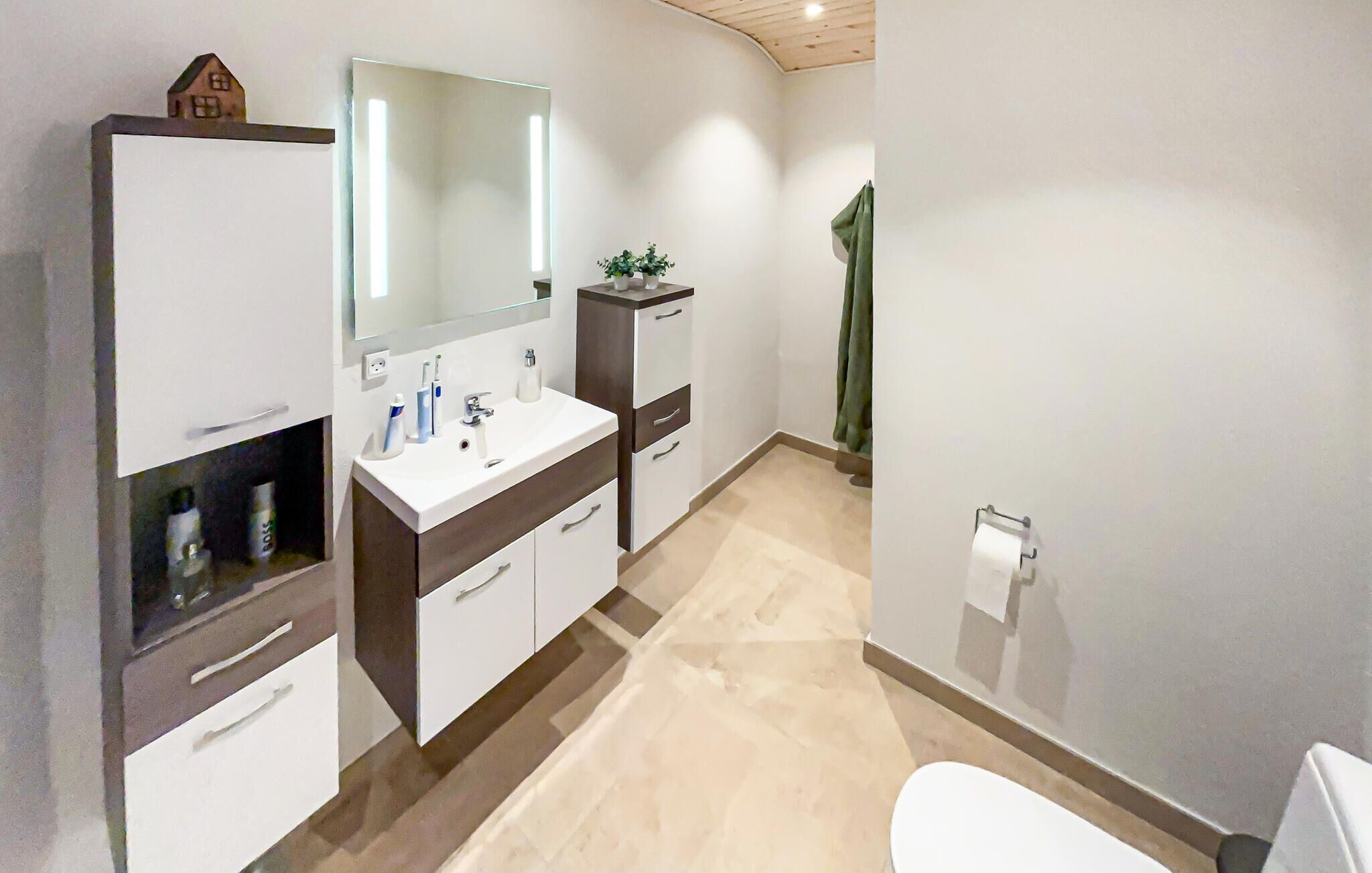 A modern bathroom with a white sink, mirror, and toilet. There is a small plant on the counter and a towel rack on the wall.