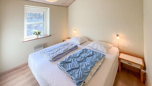 Ein Einzelbett mit weißer Bettwäsche und einer blauen Decke, zwei Nachttische, ein Fenster mit Blick auf Bäume und eine Wandleuchte.