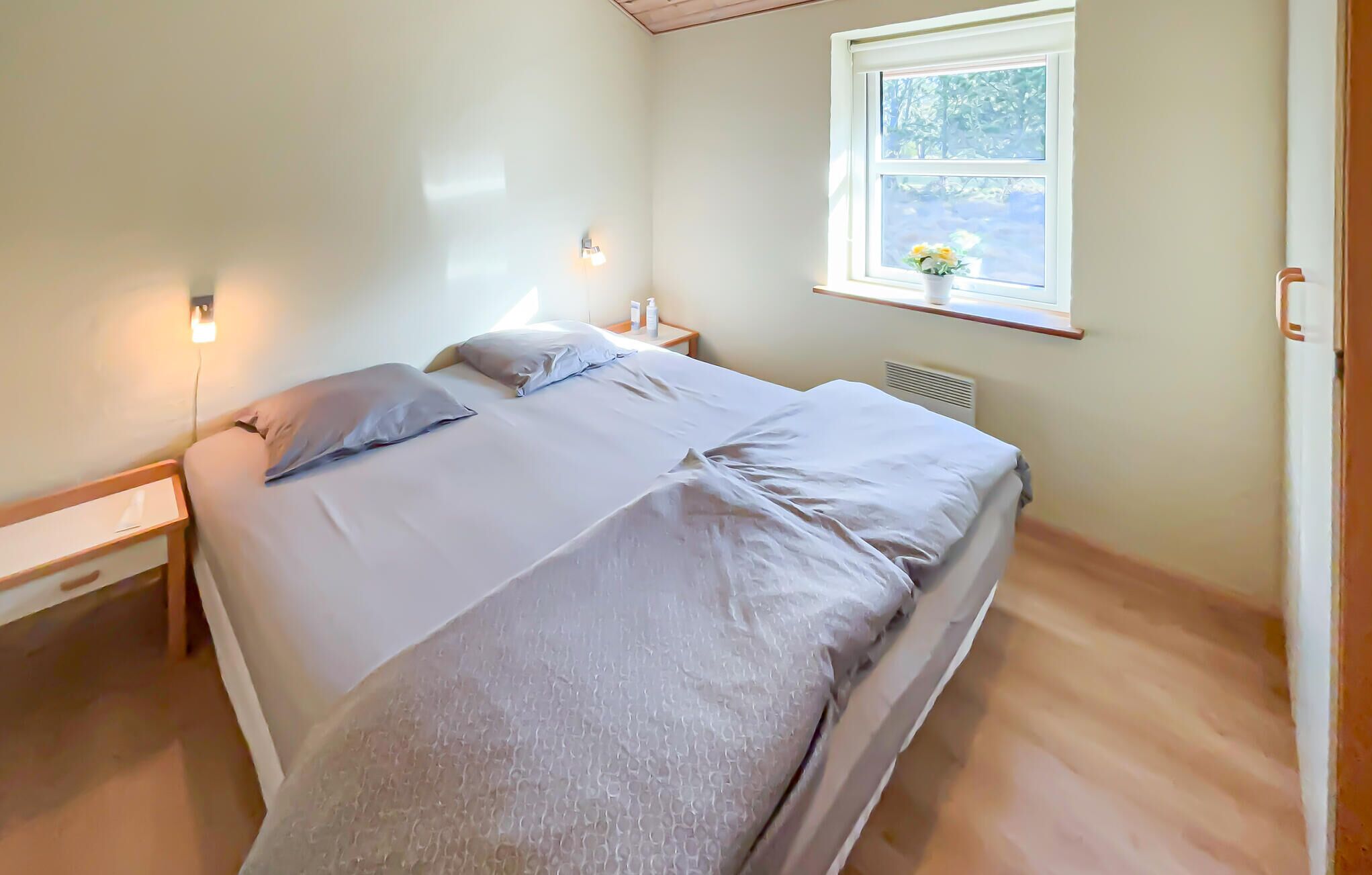 Un dormitorio con cama, mesitas de noche, ventana con vistas y una lámpara de pared.