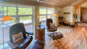 Ein Zimmer mit zwei Ledersesseln, einem Holztisch und Blick auf eine Terrasse durch große Fenster.