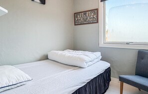 Un dormitorio con cama, una silla, un ventanal y un adorno en la pared.