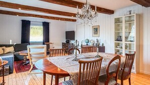 Een eetgedeelte met een houten tafel en stoelen, een kroonluchter en een boekenkast met glazen servies.