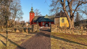 Een rode kerk met een klokkentoren, een klein geel gebouw en een pad van stenen.