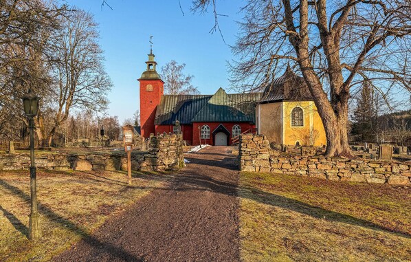 Una iglesia roja con un campanario, un pequeño edificio amarillo y un camino empedrado de piedra.