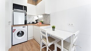 A compact kitchen with a washing machine, a microwave, and a small dining table with chairs. - GuestReady - Cosy retreat in Porto's Campanhã (Campanhã)