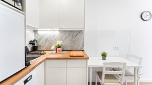 A modern kitchen with white cabinetry, a marble backsplash, a wooden countertop, and a dining area with a white table and chairs. - GuestReady - Cosy retreat in Porto's Campanhã (Campanhã)
