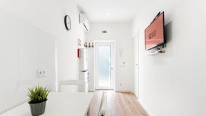 A modern hotel corridor with a wooden floor, a potted plant, a clock, an air conditioning unit, a television, and a door leading to a room. - GuestReady - Cosy retreat in Porto's Campanhã (Campanhã)