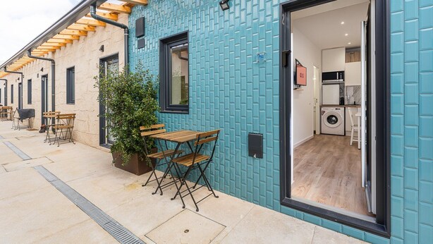 A modern building with a blue exterior, a wooden pergola, outdoor seating, and a visible laundry area. - GuestReady - Cosy retreat in Porto's Campanhã (Campanhã)