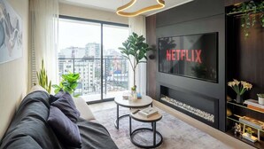 A modern living room with a large TV screen displaying 'NETFLIX,' a sofa, a coffee table, and a balcony with a city view. - Luxury Boutique Apt | Miraflores | Ocean View (Miraflores)