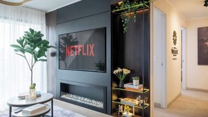 A modern living room with a large flat-screen TV mounted on a dark wall, a fireplace below, and a decorative shelf with plants and figurines. - Luxury Boutique Apt | Miraflores | Ocean View (Miraflores)