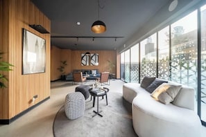 A modern living room with a sofa, ottoman, and coffee table, wooden paneling, and large windows. - Premium Apartment with pool in Larco, Miraflores. (Miraflores)