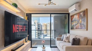 Un salon moderne doté d’un grand téléviseur à écran plat, d’un canapé, d’une table basse et d’un balcon offrant une vue sur la ville.