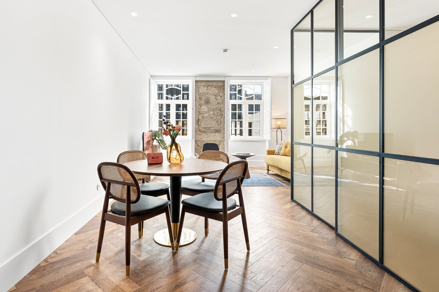 Un coin repas avec une table ronde, quatre chaises, un vase de fleurs et un canapé en arrière-plan.
