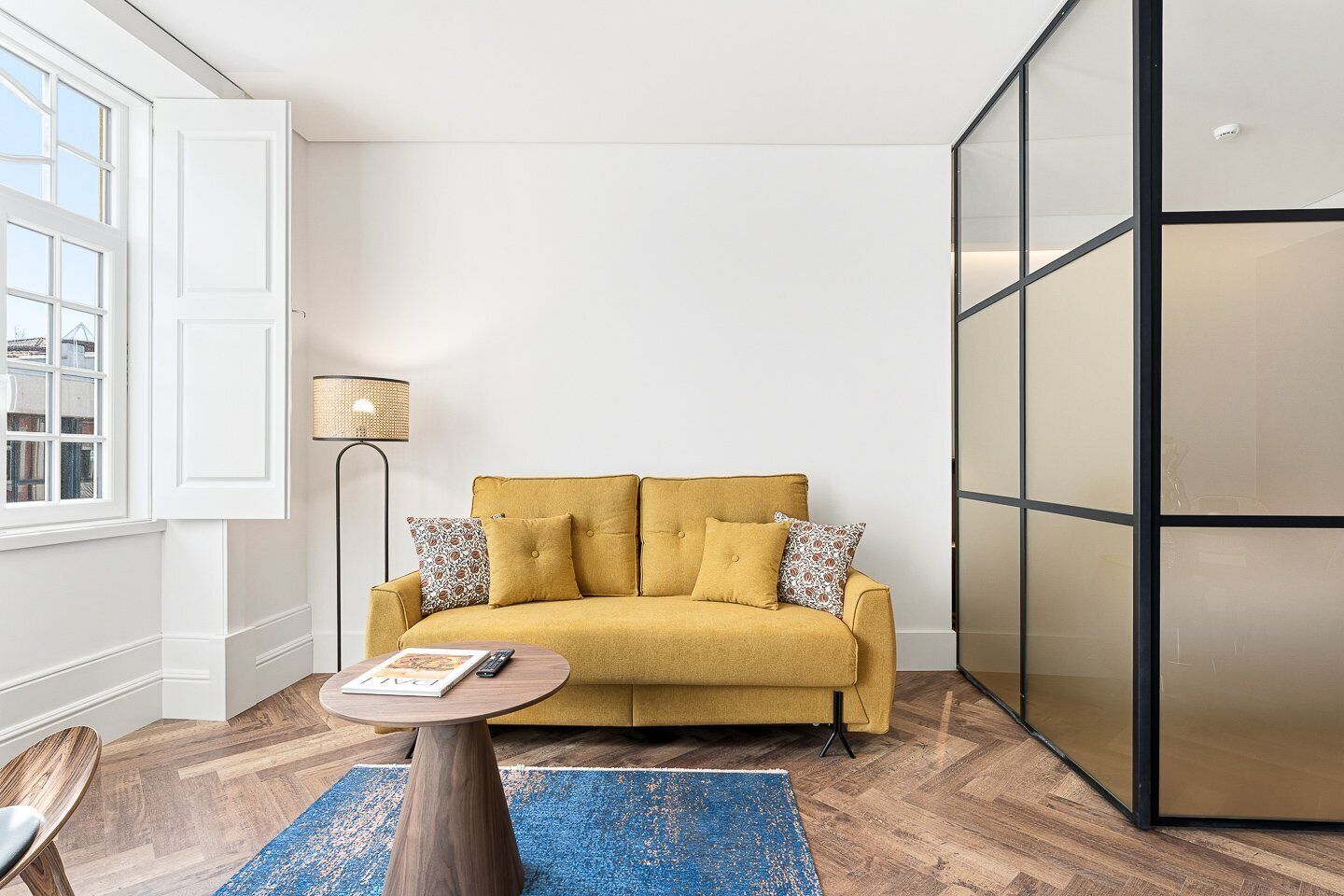 A living room with a sofa, a coffee table, a lamp, and a large window.