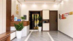 Een hotel receptie met een houten balie, een beeld, een bord en een potplant.