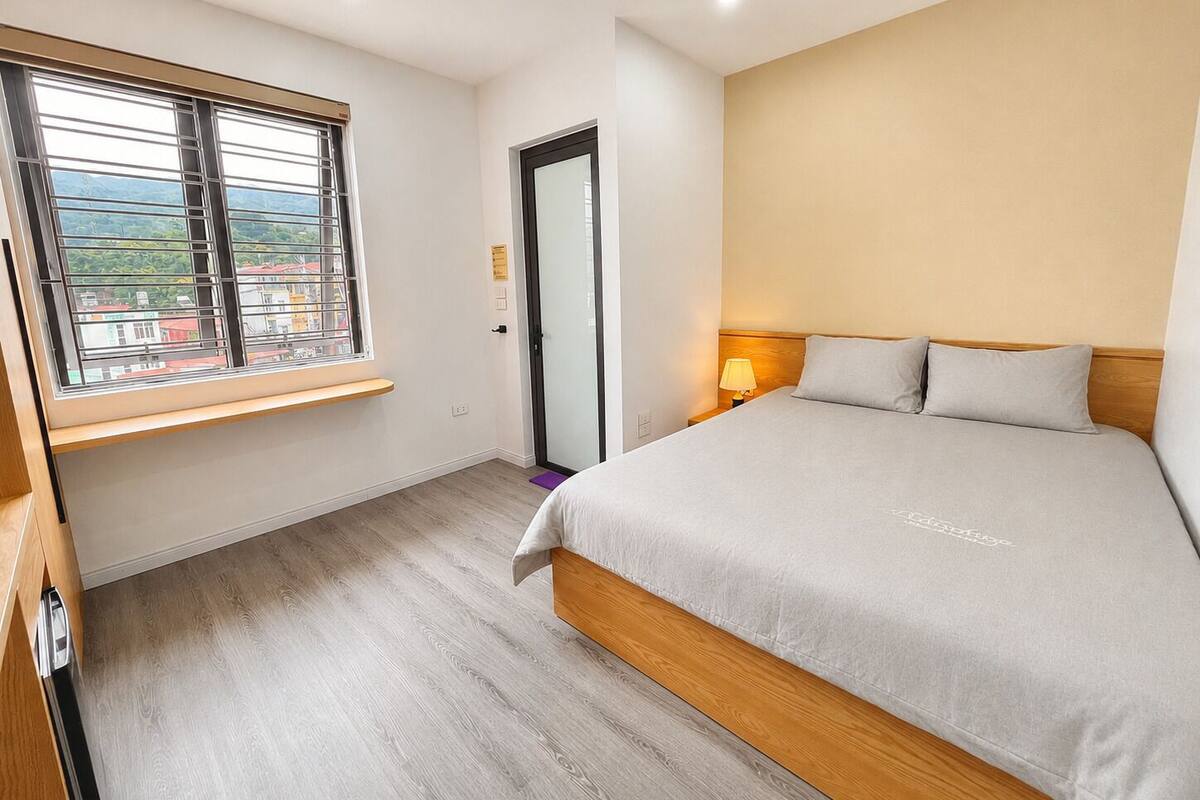 Een slaapkamer met een bed, een raam met uitzicht, een deur en een nachtkastje met een lamp.