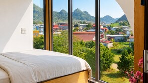Een slaapkamer met een groot raam, een bed en uitzicht op een stad en bergen.