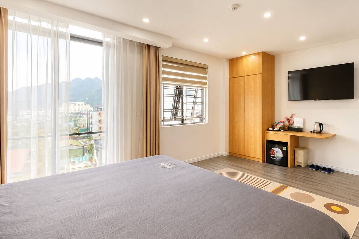 Een hotelkamer met een bed, een televisie, een klein bureau met een waterkoker en uitzicht op de stad.