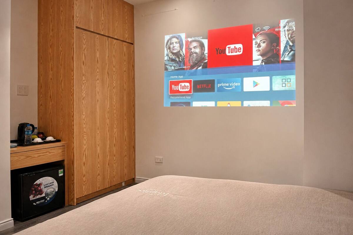 Een slaapkamer met een bed, een houten garderobe en een wandgemonteerde televisie die streamingdiensten toont.