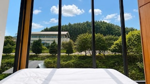 Een kamer met een bed, grote ramen en uitzicht op een gebouw en bomen.