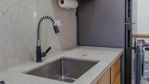 A kitchen with a granite countertop, a stainless steel sink, a black faucet, and a refrigerator. - Pool, BBQ & a Short Walk to the Malecon (La Paz)