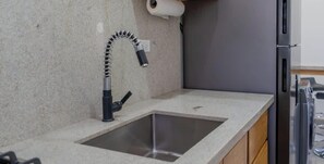 A kitchen with a granite countertop, a stainless steel sink, a black faucet, and a refrigerator. - Pool, BBQ & a Short Walk to the Malecon (La Paz)