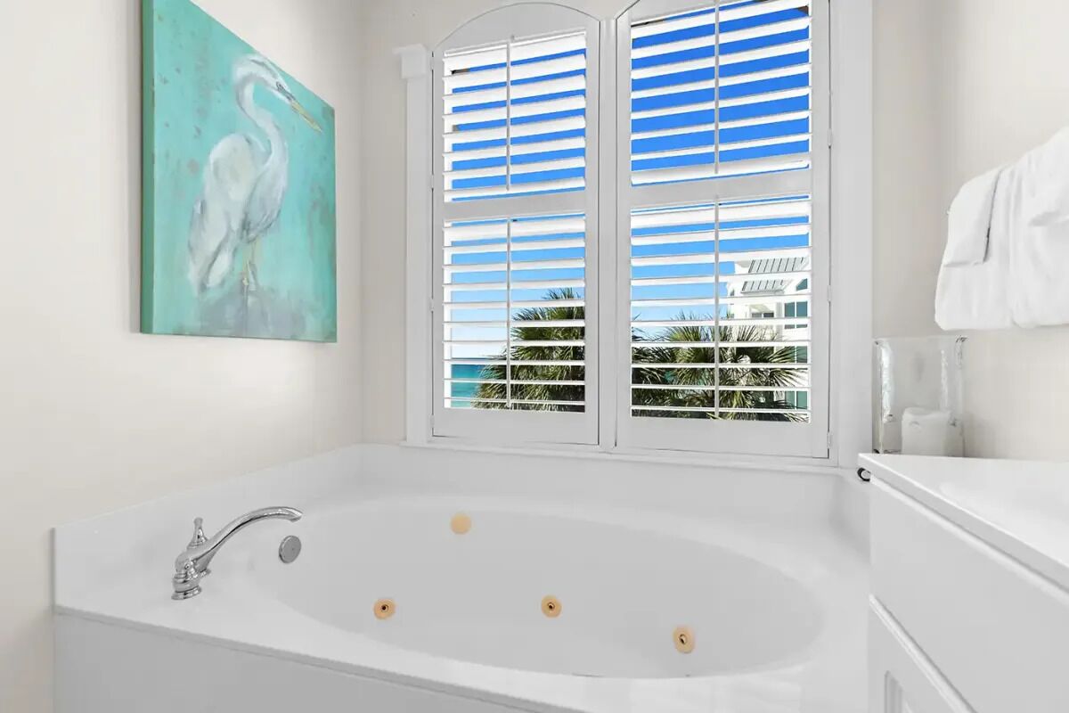 Un baño con una bañera blanca, una ventana con persianas blancas y un cuadro en la pared.