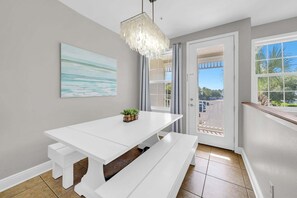 A white dining table with benches, a hanging light fixture, a painting on the wall, and a door leading outside. - Awesome 4 Bedroom overlooking Pool / Easy Beach Access (Santa Rosa Beach)