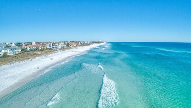 An aerial view of a beach with clear turquoise waters, a sandy shore, and buildings along the coastline. - Awesome 4 Bedroom overlooking Pool / Easy Beach Access (Santa Rosa Beach)
