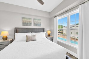 A bedroom with a large bed, two bedside lamps, a headboard, and a view of a swimming pool through a window. - Awesome 4 Bedroom overlooking Pool / Easy Beach Access (Santa Rosa Beach)
