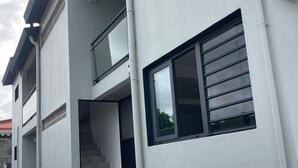 Ein modernes Gebäude mit Flachdach, einer Treppe, die zu einer oberen Etage führt, und einem großen Fenster mit horizontalen Jalousien.