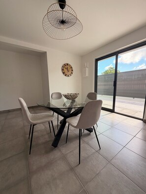 Een eetruimte met een glazen tafel, vier stoelen, een decoratieve schaal, een wandklok en een plafondlamp.