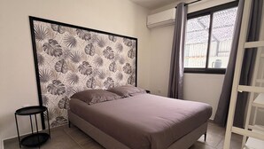Ein Schlafzimmer mit einem Bett, einem kleinen runden Tisch, einem Fenster mit Vorhängen und einer Wand-Klimaanlage.