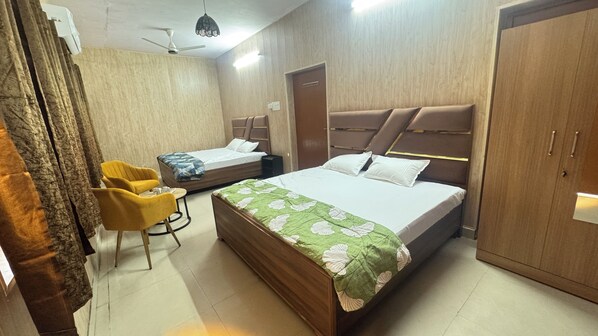A hotel room with a large bed, a smaller bed, a wardrobe, a desk, and a chair. - Devashish Homestay (Varanasi)