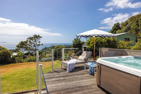 Une terrasse en bois avec un jacuzzi, des chaises longues et une vue sur l’océan.